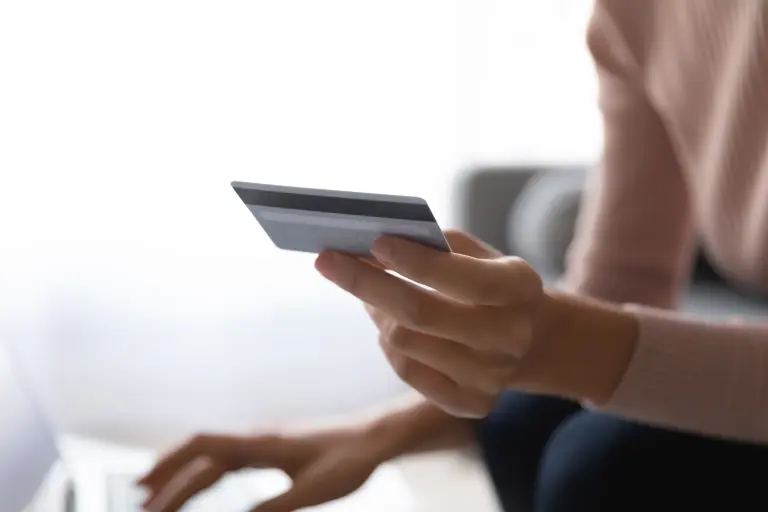 Woman sitting on couch, holding debit card shows to ATM for balance check