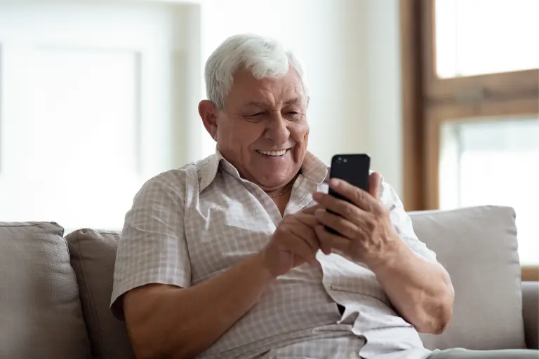 A senior gentleman using a smartphone while seated on a sofa means check account balance in Bank of India via SMS