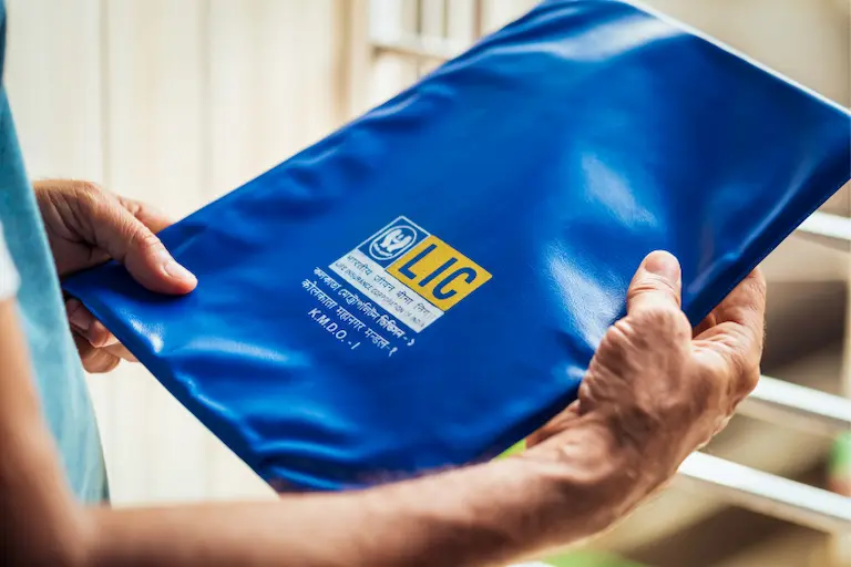 1. A man stands holding a blue bag, which is covered in a matching blue fabric, showcasing Benefits of Becoming an LIC Agent 