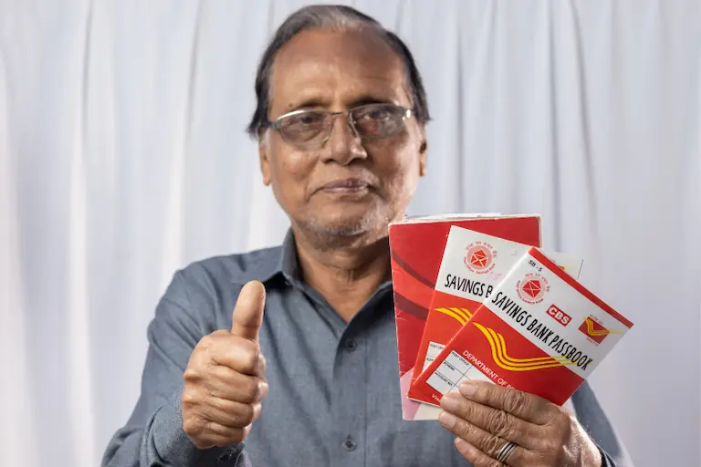 A man raises two books while giving a thumbs up, showcasing his approval and excitement for the post office book for SCSS